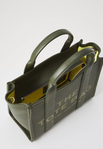 Groene gestructureerde leren totebag met dubbele handgrepen, gele binnenkant en gouden ritsdetail. De voorkant heeft grote bedrukte tekst.