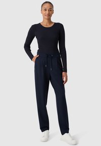 Top a maniche lunghe a coste blu navy abbinato a pantaloni larghi blu navy con cintura elastica, indossato con sneakers bianche.