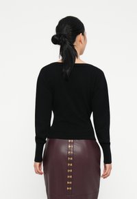 Sweater preto de mangas longas e decote largo, combinado com uma saia de couro burgundy com detalhe de botão dourado.