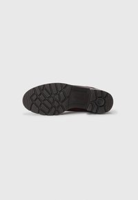 Suela de zapato de goma negra con un patrón de agarre texturizado, que presenta un borde redondeado y un estampado de logotipo en la zona del talón.