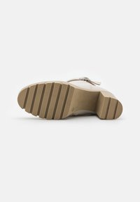 Sole di scarpa beige con texture zigrinata, caratterizzata da una forma arrotondata, materiale robusto e tacco elevato. Linee lisce e pulite senza decorazioni.