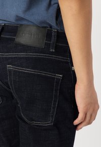 Dark indigo jeans with a textured finish, five-pocket design, and a black leather label on the waistband marked "ONLY & SONS."