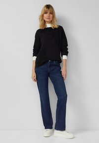 Maglione nero con polsini bianchi, abbinato a jeans blu a gamba dritta e sneakers bianche. Design semplice e vestibilità casual.