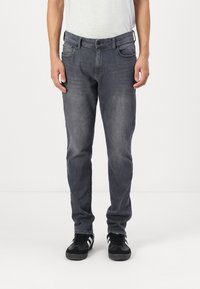 Grå denimjeans med rett benklipp, fem lommer, subtil slitasje og glidelås, brukt med svarte sneakers.