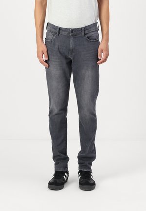 Grå denimjeans med rett benklipp, fem lommer, subtil slitasje og glidelås, brukt med svarte sneakers.