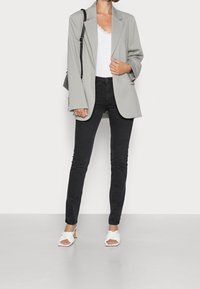 Vaaleanharmaa bleiseri, valkoinen pitsireunainen toppi, mustat kapealahkeiset farkut, valkoiset lohkopohjakorkokengät, joissa kiertyvä hihnallinen yksityiskohta. Yksinkertainen ja siisti muotoilu.