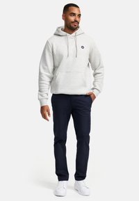 Sudadera gris claro con un bolsillo frontal y cordón ajustable. Combinada con pantalones navy y zapatillas blancas, mostrando un conjunto casual.