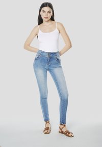 Blauwe spijkerbroek met hoge taille en een licht vervaagde look, voorzien van twee voorzakken en een sluiting met vier knopen. Draagt bij een wit tanktopje.