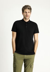 Polo negro con cuello y tapeta de tres botones, fabricado en una tela suave; combinado con pantalones cargo verde oliva.