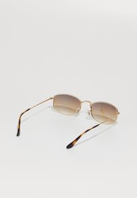 Lunettes de soleil carrées avec une monture dorée, des verres à dégradé brun et des branches au motif écaille de tortue, sur une surface blanche.