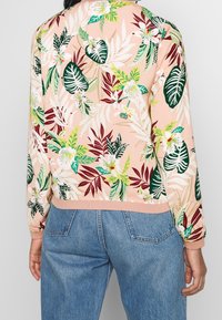 Sudadera ligera de color rosa con un vibrante patrón de hojas y flores tropicales, de mangas largas y con un dobladillo acanalado, combinada con denim.