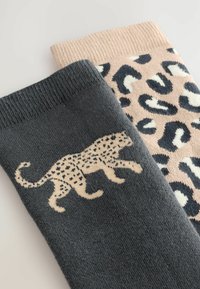 Donkergrijze sok met een beige luipaardgrafiek; lichtroze sok met zwarte en beige luipaardvlekken; beide hebben geribde boorden en een zachte textuur.