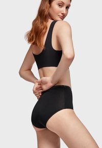 Soutien-gorge noir et ensemble de culottes taille haute. Le soutien-gorge possède des bretelles larges ; la culotte a une finition lisse avec un bord festonné sur la taille.
