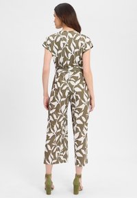 Blumenmuster-Jumpsuit in Olivgrün und Weiß. Kurze Ärmel, weit geschnittene Hosenbeine, mit einem Gurt in der Taille, aus einem glatten, leichten Stoff hergestellt.