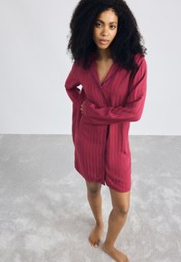Camicia da notte magenta con righe verticali, maniche lunghe e colletto a contrasto. Tessuto morbido con una vestibilità ampia e lunghezza fino a metà coscia.