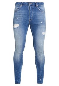 Jeans ajustados de mezclilla azul deslavada con detalles desgastados, incluyendo rasgaduras y salpicaduras de pintura. Diseño clásico de cinco bolsillos y cremallera.