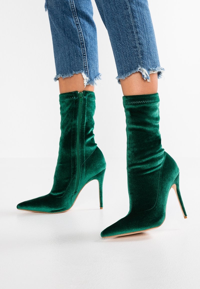 Bottes chevilles en velours vert avec un bout pointu, un talon stiletto haut et une fermeture éclair. Le design présente une texture froncée sur le dessus.
