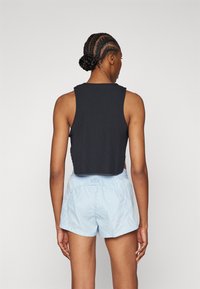 Top corto negro con diseño acanalado y sin mangas, combinado con pantalones cortos azul claro que presentan un logo en la cinturilla y sutiles rayas verticales.