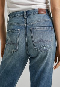 Kratke jeans hlače v svetlo modri barvi z obrabljenim zaključkom, z dvema zadnjima žepoma, detajli šivanja in rjavim usnjenim oznakama na pasu.