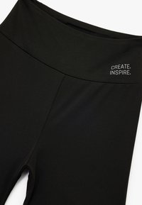 Zwarte leggings met een hoge tailleband, met een gladde textuur en de opdruk "CREATE. INSPIRE." aan de bovenlinkerkant.