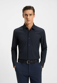 Marineblauwe shirt met lange mouwen, voorzien van een klein wit en lichtblauw geometrisch patroon, met een button-down kraag en een slim fit ontwerp. Zwarte riem.