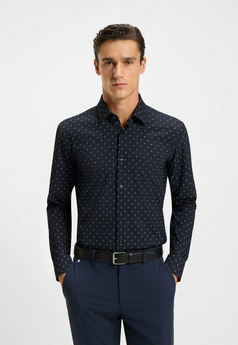 Marineblauwe shirt met lange mouwen, voorzien van een klein wit en lichtblauw geometrisch patroon, met een button-down kraag en een slim fit ontwerp. Zwarte riem.