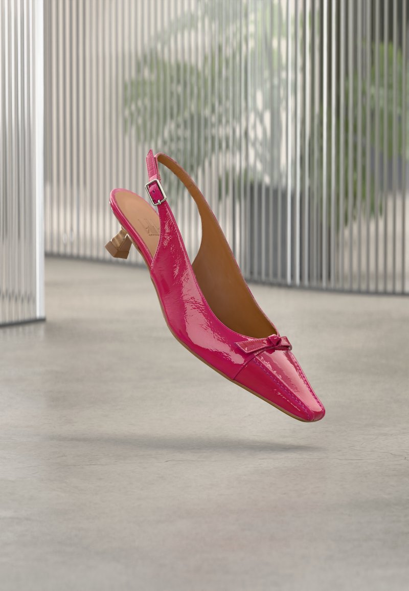 Γυαλιστερό ροζ παπούτσι με λουρί στο πίσω μέρος, χαμηλό ξύλινο τακούνι και μικρό διακοσμητικό φιόγκο στην αιχμηρή μύτη, τοποθετημένο πάνω σε θαμπό εσωτερικό φόντο.