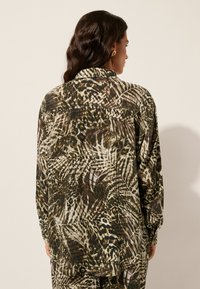Camisa de manga larga en una tela ligera y transparente con una mezcla de patrones de animales y plantas en tonos tierra de verde, marrón y crema.