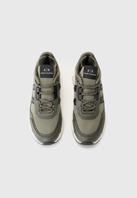 Green athletic shoes with a textured fabric upper, black accents, and a white sole featuring a distinctive design. Laces integrated into the structure.