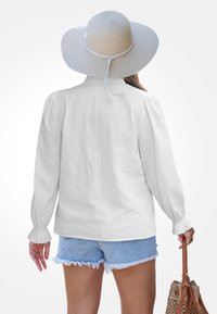 Biała koszula z długim rękawem i bufiastymi ramionami, w połączeniu z jasnoniebieskimi szortami dżinsowymi. Na głowie noszona szerokozaczkowa słomkowa kapelusz, a w ręku trzymana brązowa torebka.