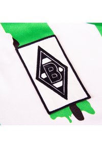 Zwart-witte diamantvormige "B" logo patch op een witte stof met groene en zwarte abstracte penseelstreken.