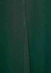 Tessuto a maglia verde con una consistenza liscia e sottili variazioni di tonalità, che presenta un dettaglio di cucitura verticale.