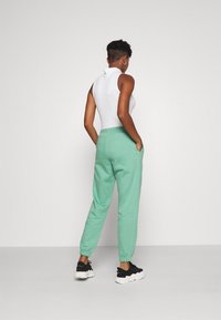 Lichtgroene joggers met elastische boorden en zijzakken, gecombineerd met een witte mouwloze top en zwarte sportschoenen, gezien van achteren.