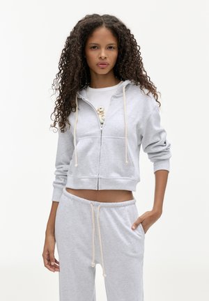 Sweat à capuche gris coupé en tissu doux, doté d'une fermeture éclair avant, d'une capuche avec cordon de serrage et de poches kangourou, associé à un jogging gris assorti.