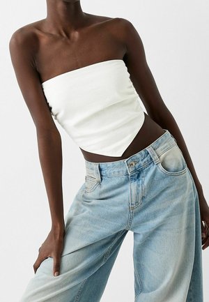Weißes trägerloses Top mit tailliertem Oberteil und spitzem Saum. Kombiniert mit hellblauen High-Waist-Jeans, entspannter Passform und ausgewaschenem Look.