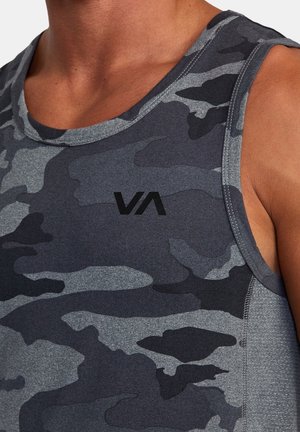 Zbliżenie na osobę noszącą bezrękawnik w ciemnoszarym i czarnym wzorze moro z małym logo "VA" na piersi.