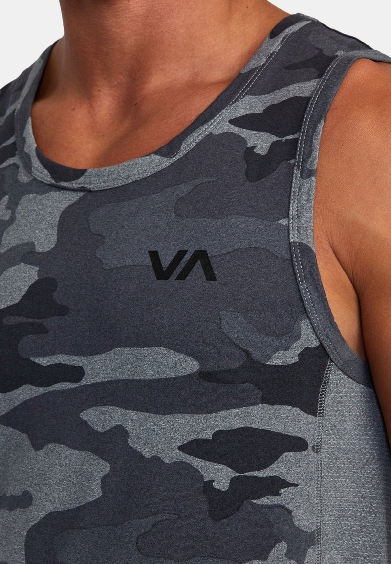 Gros plan sur une personne portant un haut de sport sans manches, à motif camouflage gris foncé et noir, avec un petit logo "VA" sur la poitrine.