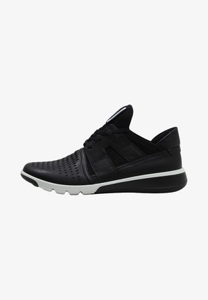 Chaussure de sport noire avec embout perforé, design à lacets, semelle blanche et noire, et col rembourré, vue de côté.