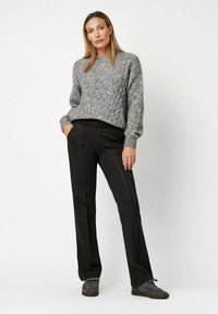 Pull en maille gris avec un motif texturé et des poignets côtelés, associé à un pantalon noir ajusté et des baskets grises, créant un look décontracté.