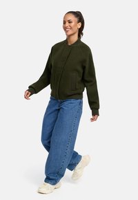 Grön bomberjacka i ullblandning med ribbade ärmslut och nederkant, med knäppning. Matchas med löst sittande blå denimjeans och sneakers.