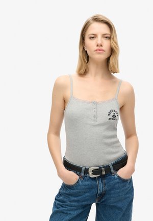 Szary, prążkowany top bez rękawów z koronkowym wykończeniem, z guzikami z przodu oraz nadrukowanym logo. W połączeniu z niebieskimi dżinsami o wysokim stanie i czarnym paskiem.