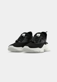 Black mesh sneakers with white chunky soles, elastic toggle laces, and pull tabs on a plain light background.