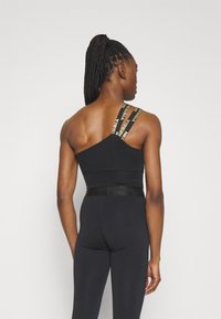 Top atlético negro con diseño asimétrico, que presenta una tira ancha con un logotipo y una cintura ajustada. Combinado con leggings negros a juego.