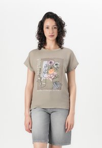 T-shirt beige clair à manches courtes avec un motif floral en ligne et du texte. Tissu en coton doux avec une coupe décontractée. Assorti avec un short en denim gris.
