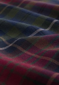 Tartan tyg i mörkblå, grön och vinröd med rutor som har tunna vita linjer. Texturen verkar mjuk och vävd.