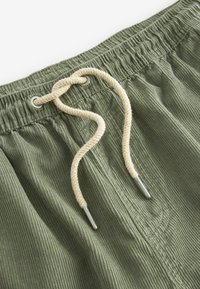 Olijfgroene corduroy short met een elastische tailleband, voorzien van een romige koord en metalen punten. Gestructureerd oppervlak met verticale ribbels.