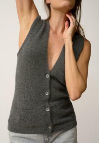 Chaleco de punto gris con un escote en V profundo, cuatro botones en la parte delantera y bolsillos frontales, hecho de una tela suave y de diseño ajustado.