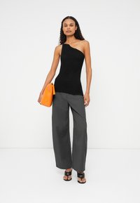 Top tricotat negru cu un umăr, asortat cu pantaloni largi gri și o geantă texturată portocalie; modelul poartă sandale negre cu barete.