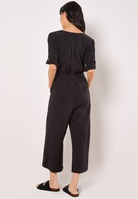 Mono ligero y negro con un corte relajado, cintura elástica, mangas enrollables y pata recortada. Textura suave, diseño minimalista.