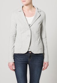 Szary, dopasowany żakiet z kołnierzem typu rewers, dwoma guzikami i przednimi kieszeniami, wykonany z miękkiej tkaniny, noszony na białej koszuli i ciemnych dżinsach.